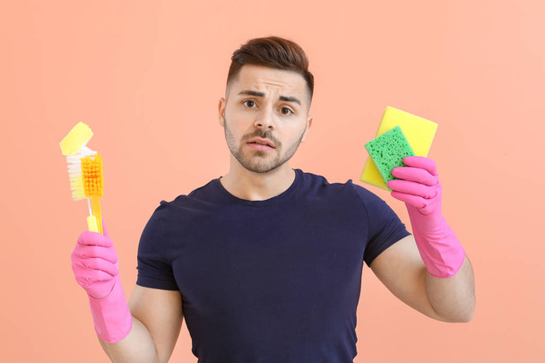 Грустный молодой человек с чистящими средствами на цветном фоне
 - Фото, изображение