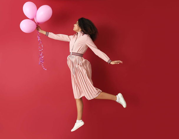 Retrato de mujer afroamericana saltando con globos de aire sobre fondo de color
 - Foto, imagen