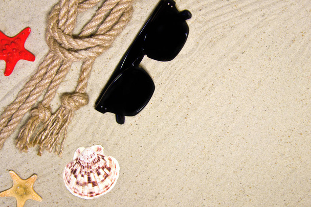 Conchas marinas y decoración de cuerdas náuticas sobre fondo de arena con gafas de sol
 - Foto, imagen