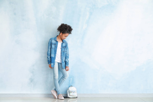 Stylish African-American girl in jeans clothes and with backpack near color wall - Фото, изображение