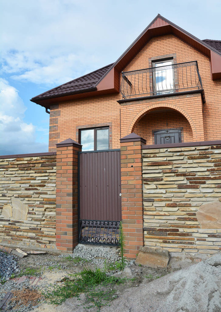 Maison moderne de luxe en brique en construction avec clôture en pierre et porte d'entrée en métal
 - Photo, image