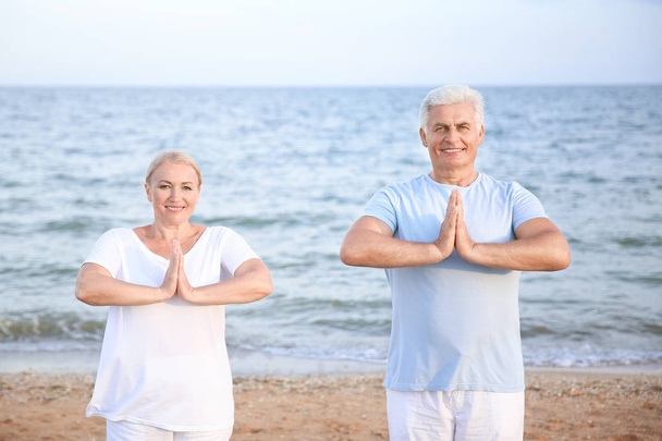 Volwassen paar beoefenen van yoga op zee Resort - Foto, afbeelding