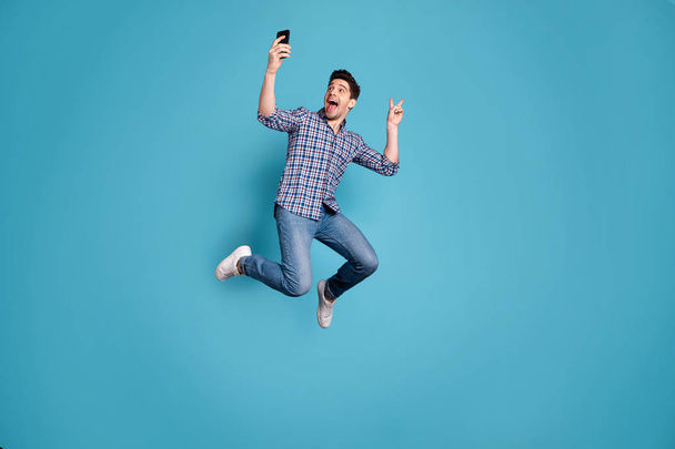 Full length body size view photo of amazed crazy funky youth make photo v-sign free time weekend holidays dream dreamy wear checked shirt jeans legs sneakers isolated blue background - Foto, Imagem