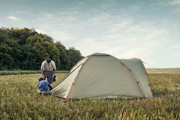Family set up tent camp at sunset, beautiful summer landscape. Tourism, hiking and traveling in nature. - Photo, Image