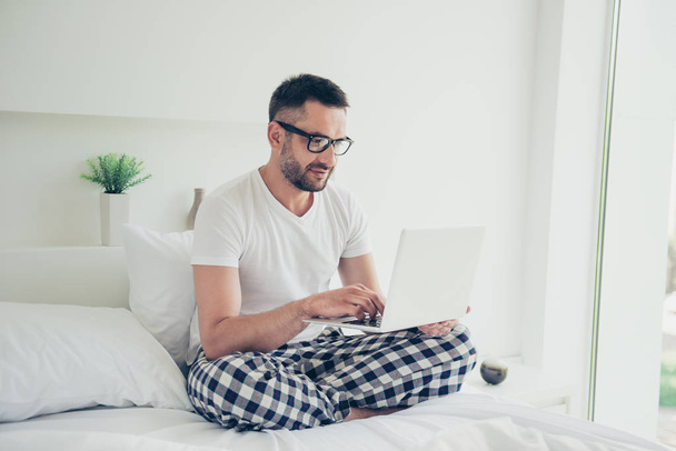 Close up photo amazing he him his guy weekend workaholic notebook writing check currency speak skype partners white nightwear sleep wear t-shirt checkered pants sitting bed bright room house indoors - Foto, Imagem