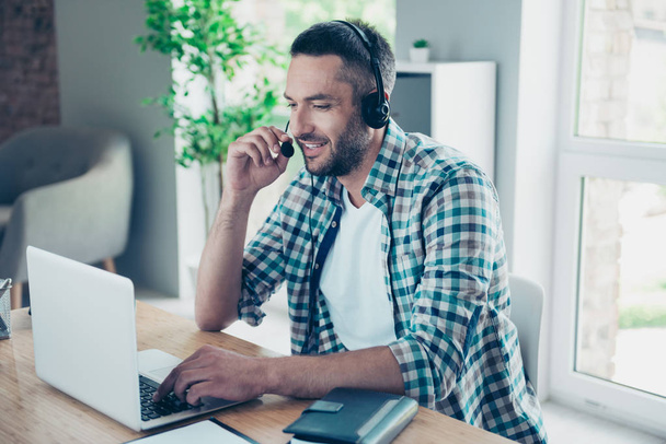 Close up side profile photo handsome he him his guy headset speak microphone customer answer questions help assist buyer call center notebook table desk sit office chair wear plaid checkered shirt - 写真・画像