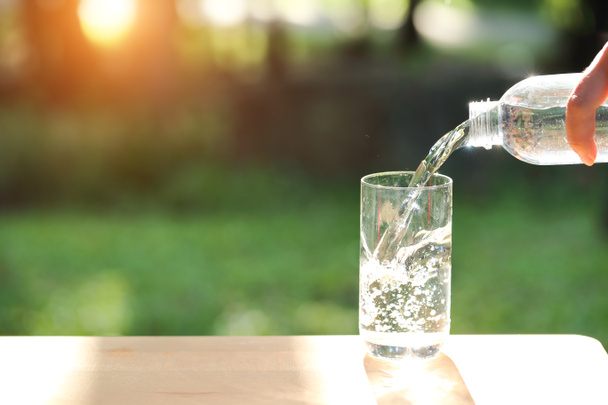 pić wodę nalewanie do pustego szkła z naturalnym zielonym tłem - Zdjęcie, obraz