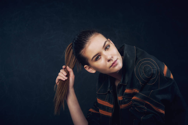 Portret van een jong mooi meisje op een donkere achtergrond. Meisje in leren jas - Foto, afbeelding
