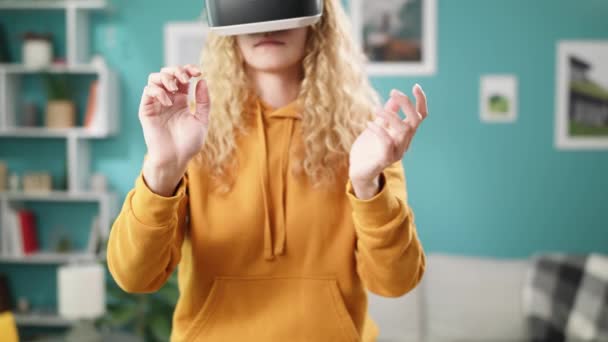 Woman in the yellow hoodie VR glasses waving hands in the cozy living room - Кадри, відео
