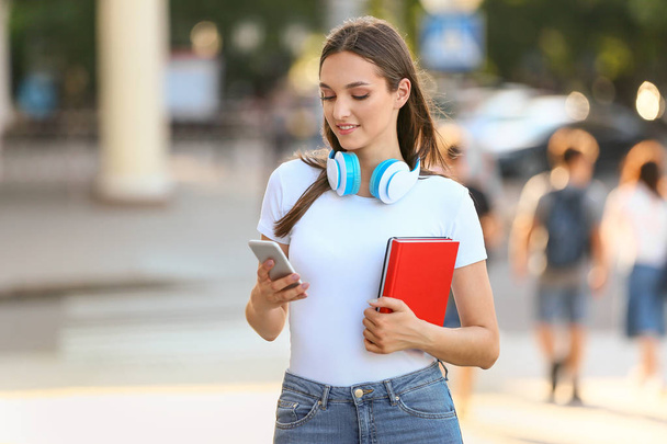 Красивая студентка с мобильным телефоном и наушниками на улице
 - Фото, изображение