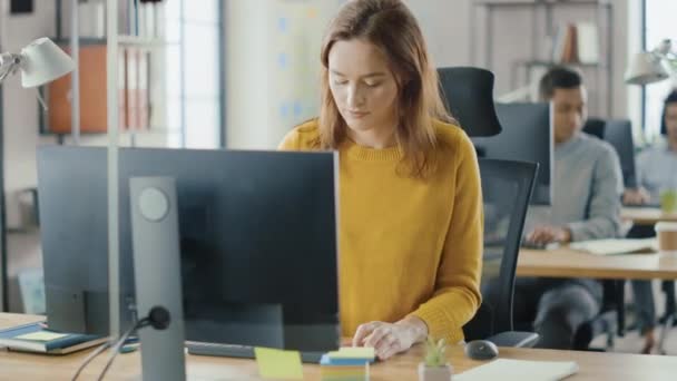 Beautiful and Smart Red Haired Female Specialist Sitting at Her Desk Works on a Desktop Computer. Bright and Modern Open Space Office with Stylish Ergonomic Furniture for Talented Creative People - Video