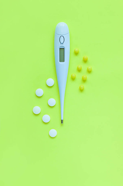 Pills and white digital thermometer on a yellow background. Flat lay, top view, minimalistic style. - Фото, изображение