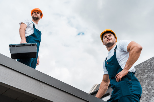 low angle view of handsome handymen in helmets against sky with clouds  - Fotoğraf, Görsel