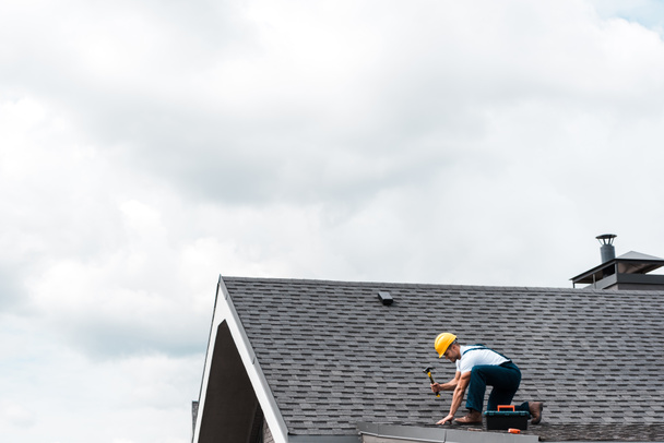 repairman in helmet holding hammer while repairing roof  - Photo, Image