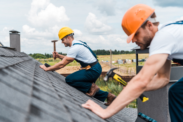 selective focus of handsome handyman repairing roof with colleague  - Photo, Image
