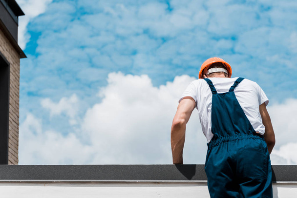 back view of repairman in helmet and uniform standing against blue sky with clouds  - Foto, imagen