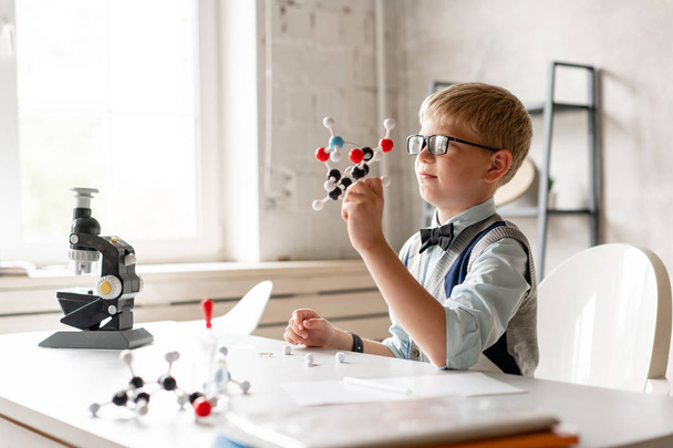 Écolier dans des lunettes tient le modèle de l'élément shemical dans les mains
 - Photo, image