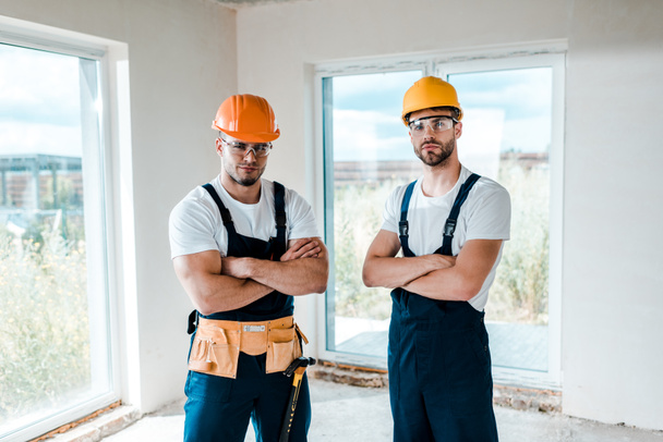 handsome handymen in helmets and goggles standing with crossed arms  - Photo, Image