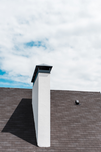cheminée blanche près des bardeaux sur le toit dans la maison contre le ciel bleu avec des nuages
  - Photo, image