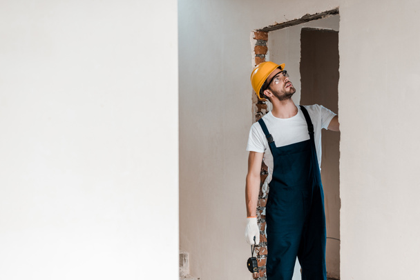 handsome repairman in gloves holding measuring tape and looking at wall  - Photo, Image