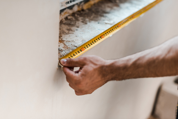cropped view of repairman measuring wall with yellow measuring tape  - Foto, imagen