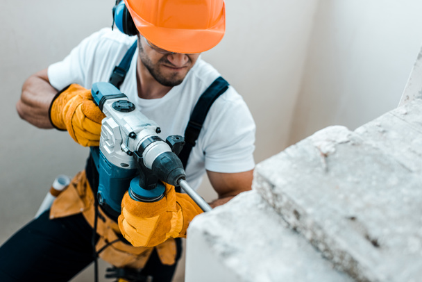 overhead view of handyman in helmet and yellow gloves using hammer drill  - Photo, Image