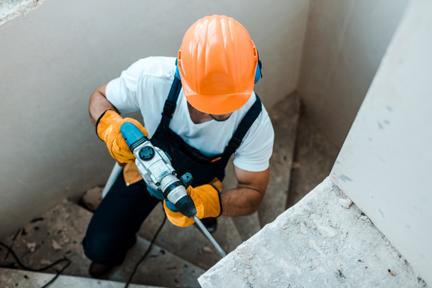 vista aérea del trabajador en guantes uniformes y amarillos con taladro de martillo
  - Foto, Imagen