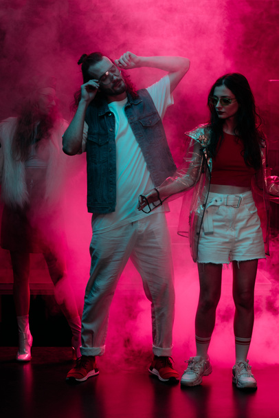 mies ja tyttö tanssivat yökerhossa neonvaaleanpunaisen savun kanssa
 - Valokuva, kuva