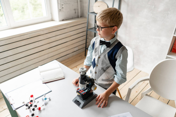 Little schoolboy in casual clothes looks in microscope - Foto, Bild