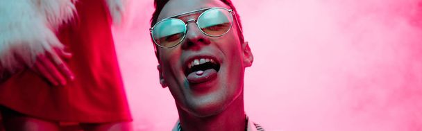 panoramic shot of man with lsd on tongue in nightclub with pink smoke - Photo, Image