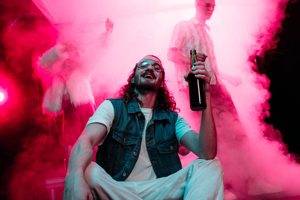 hombre feliz en gafas de sol con botella de alcohol durante rave en discoteca
 - Foto, Imagen