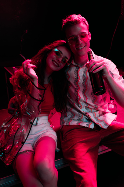 happy man with beer near girl with cigarette in nightclub during rave - Photo, Image