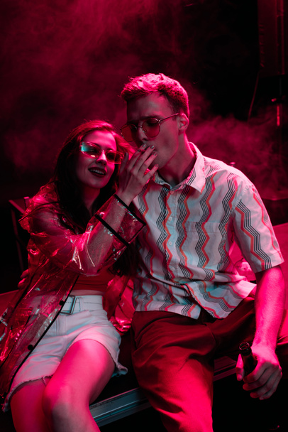 man smoking cigarette near young woman during rave party in nightclub - Фото, зображення