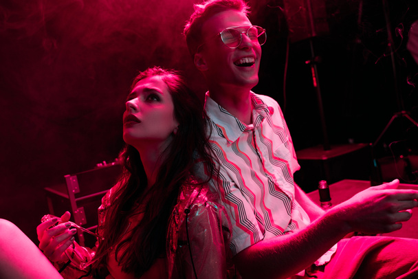 hombre y mujer joven sentados juntos durante fiesta rave en discoteca
 - Foto, Imagen