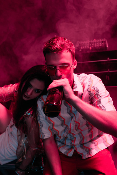 man with beer embracing girl in nightclub during rave - Foto, Imagen