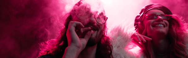panoramic shot of man smoking marijuana joint near smiling girl in nightclub - Photo, Image