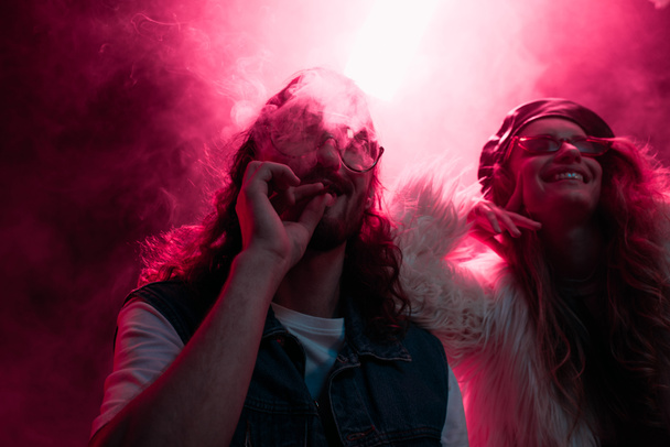 man roken marihuana gewricht in de buurt van glimlachend meisje in nachtclub - Foto, afbeelding