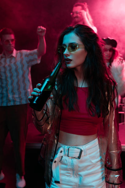 beautiful girl in sunglasses drinking beer in nightclub during rave - Photo, Image