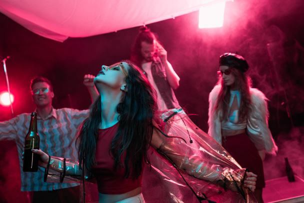 girl holding beer and dancing in nightclub with pink smoke - Foto, Imagen