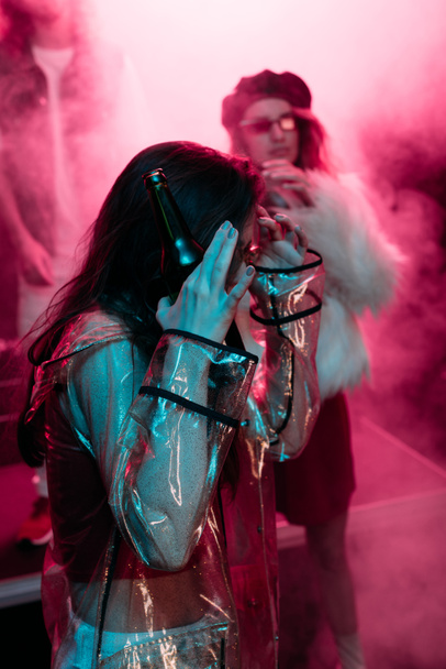 Mädchen bedeckt Gesicht beim Tanzen in Nachtclub mit rosa Rauch - Foto, Bild