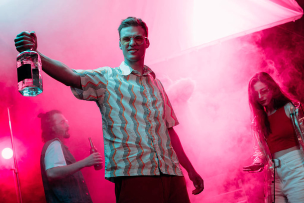 hombre guapo con botella de alcohol durante rave en discoteca
 - Foto, Imagen