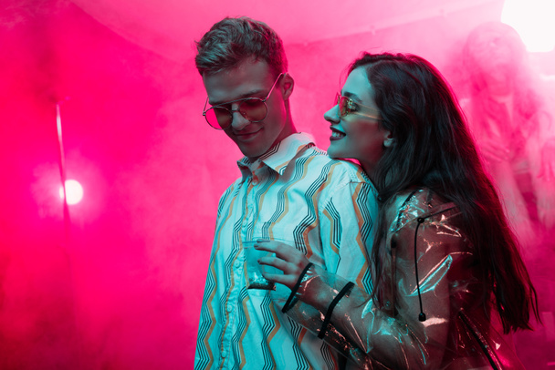 smiling girl holding weed in plastic zipper bag near man in nightclub - Photo, Image