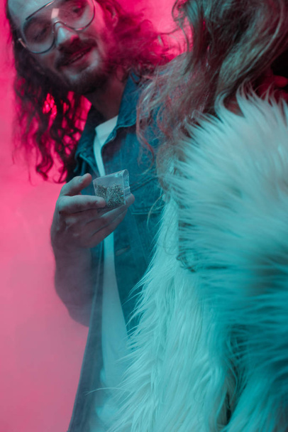 man in sunglasses giving weed in plastic zipper bag to girl in nightclub - Foto, afbeelding