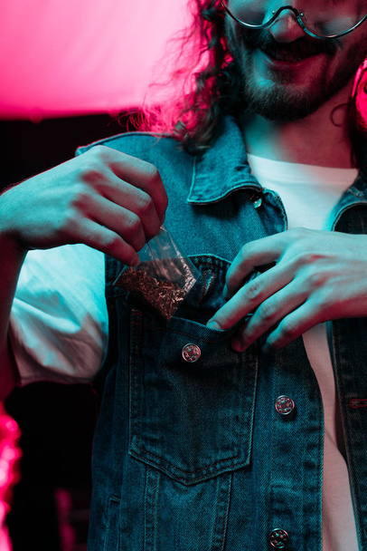 Vista recortada del hombre poniendo en bolsillo marihuana en discoteca
 - Foto, imagen