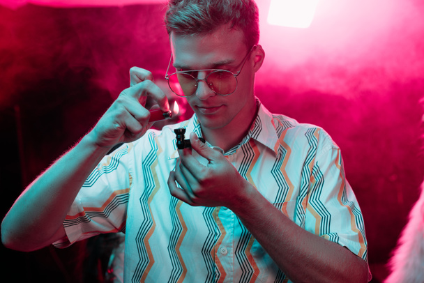 hombre guapo iluminación pipa de fumar con marihuana en discoteca
 - Foto, Imagen