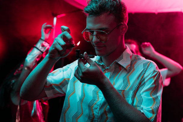 man lighting smoking pipe with marijuana in nightclub - Fotó, kép