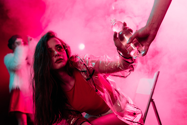 sick young woman taking bottle of water in nightclub - Foto, afbeelding