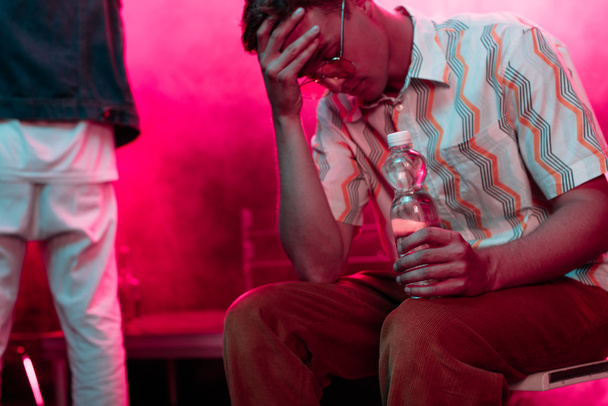 enfermo con dolor de cabeza sentado con botella de agua en el club nocturno
 - Foto, Imagen