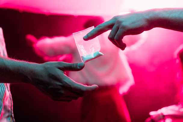 περικομμένη άποψη του ανθρώπου που περνά φάρμακα σε πλαστική τσάντα φερμουάρ σε άνθρωπο σε νυχτερινό κέντρο διασκέδασης - Φωτογραφία, εικόνα