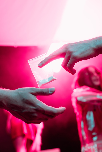 частичный вид человека, передающего наркотики в пластиковом пакете молнии мужчине в ночном клубе
 - Фото, изображение